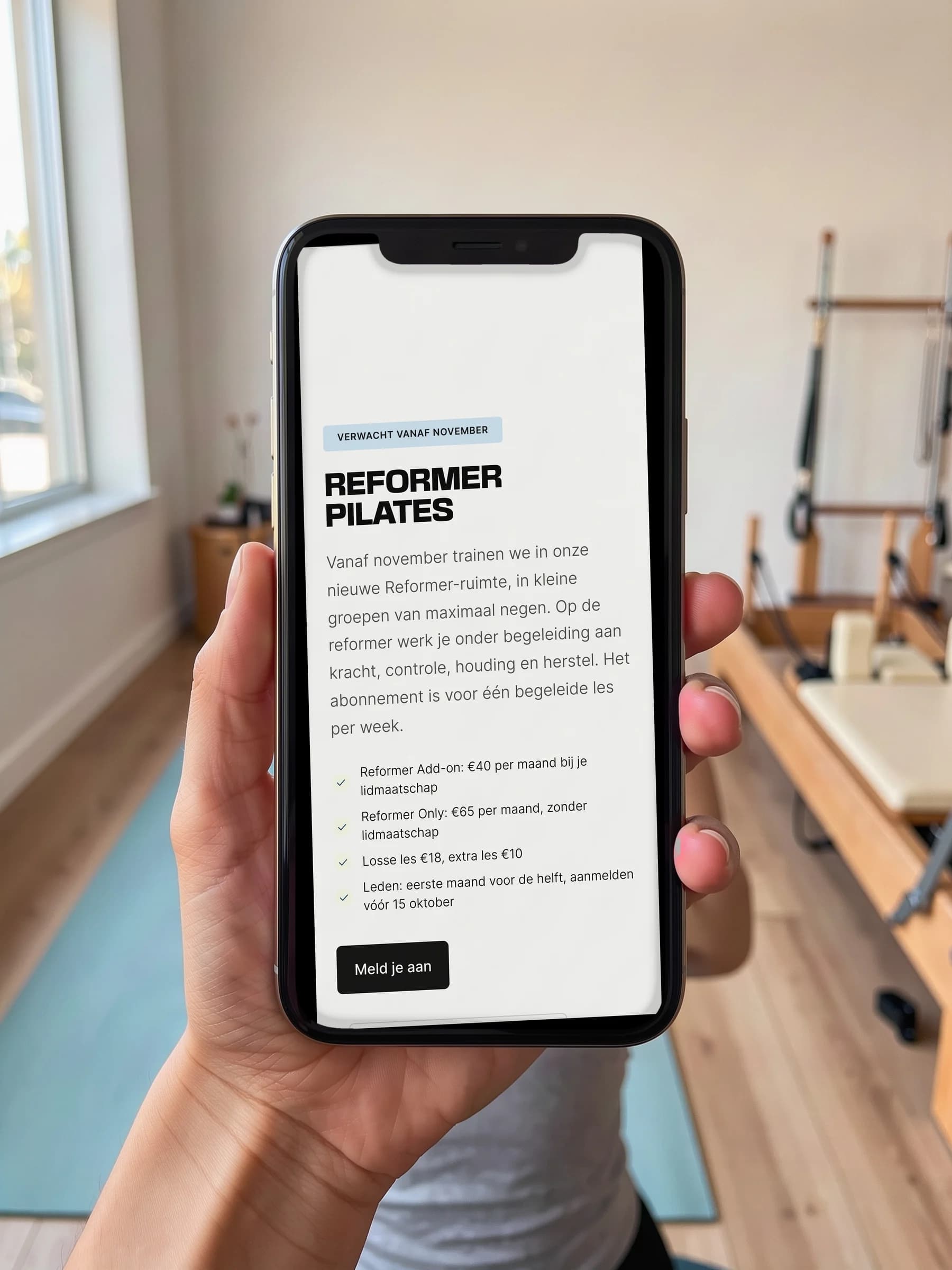 De Reformer Pilates-pagina van De Kloek Fitness op een telefoon in de hand, in een lichte studio