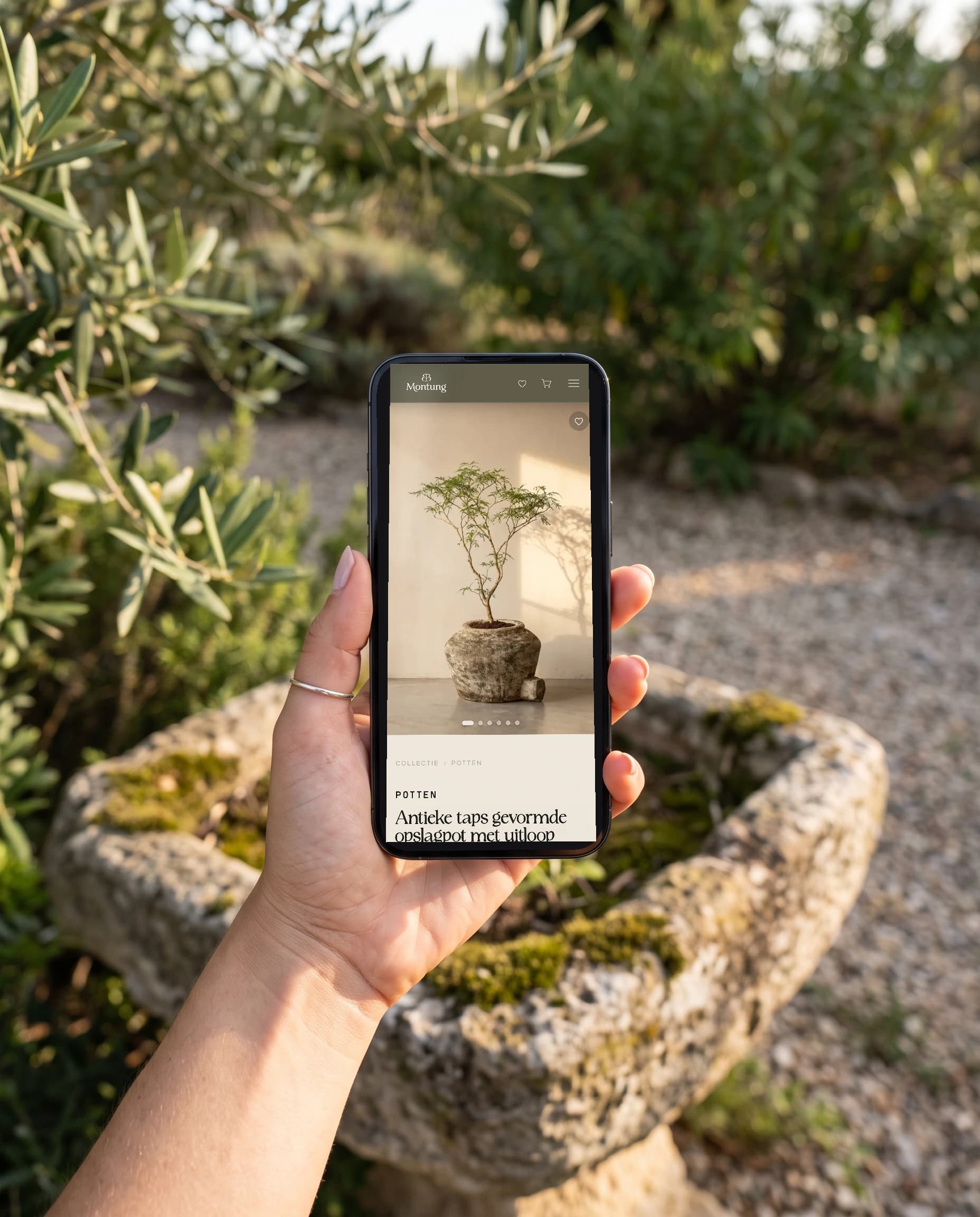 De productpagina van Montung op een telefoon in de hand, boven een oude stenen trog in een tuin