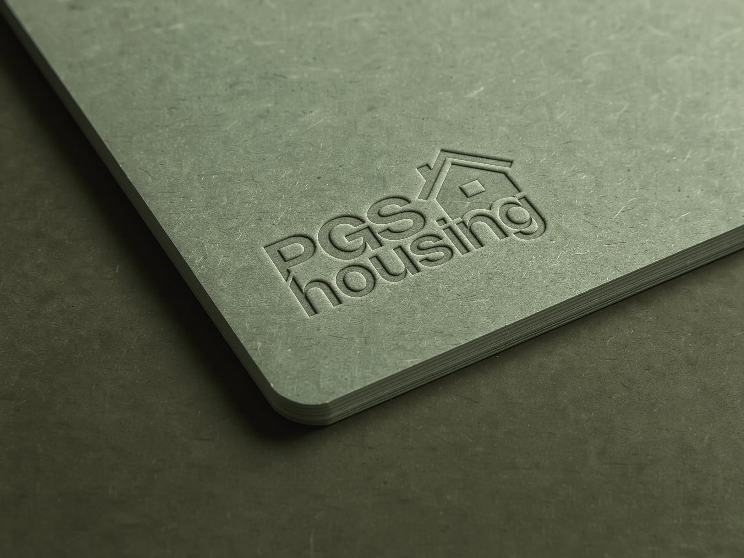 Het logo van PGS Housing blind in reliëf gedrukt op een dik saliegroen karton met ronde hoek